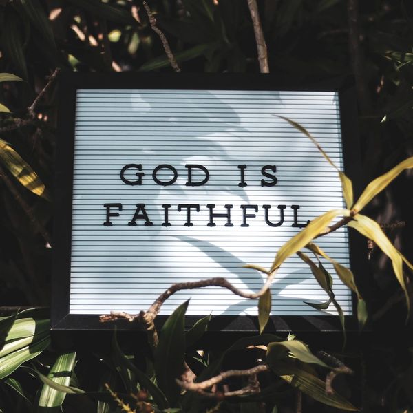 A sign reading 'God is Faithful' surrounded by green leaves.