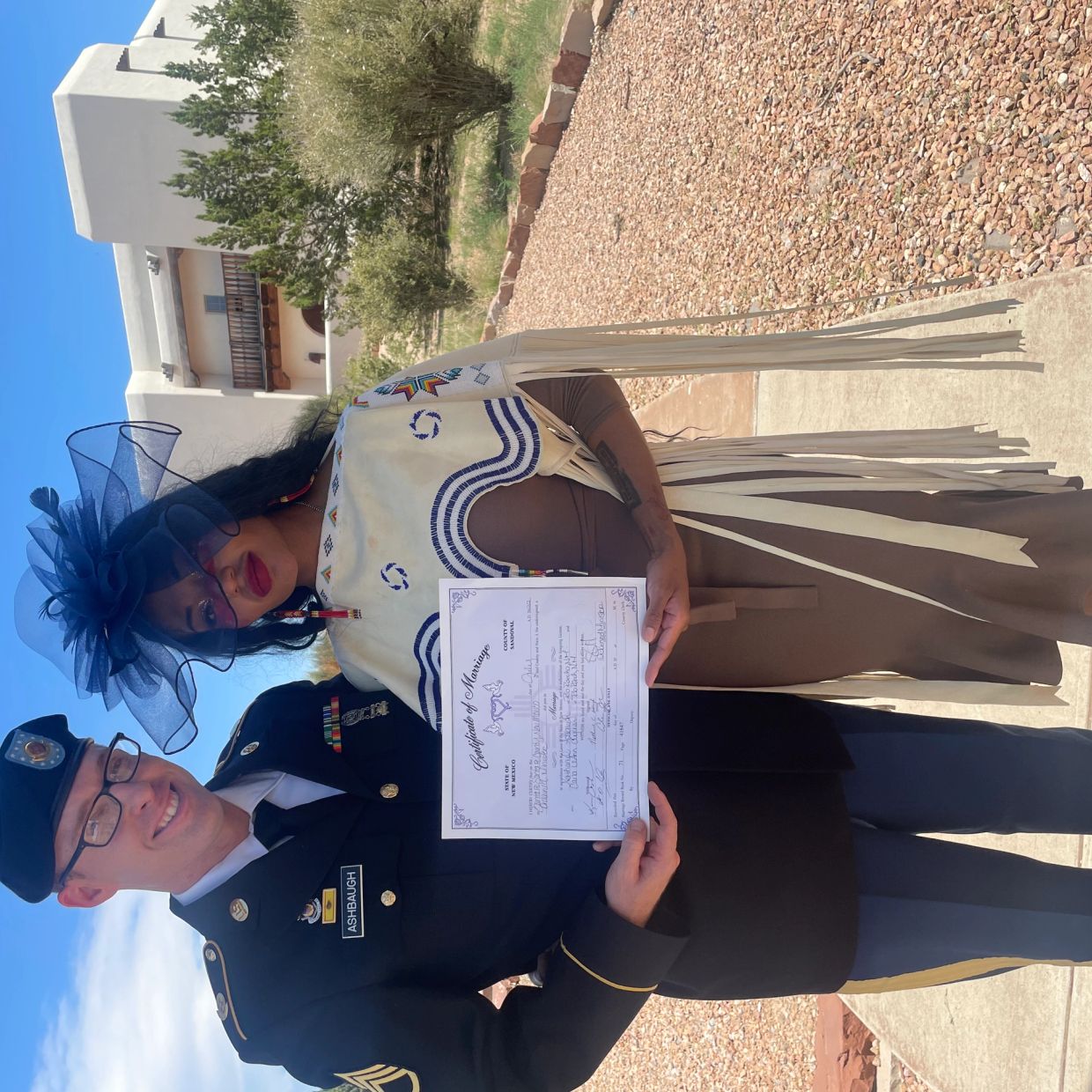 Newlywed couple proudly holding their marriage certificate outdoors.