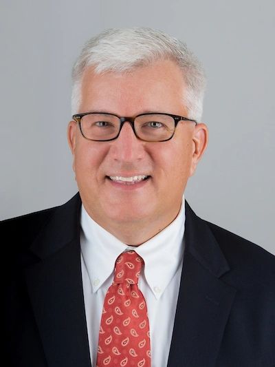 Professional headshot of a middle-aged man in glasses and a suit.