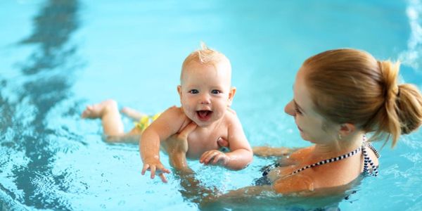 Mother holds joyful baby in swimming pool water.