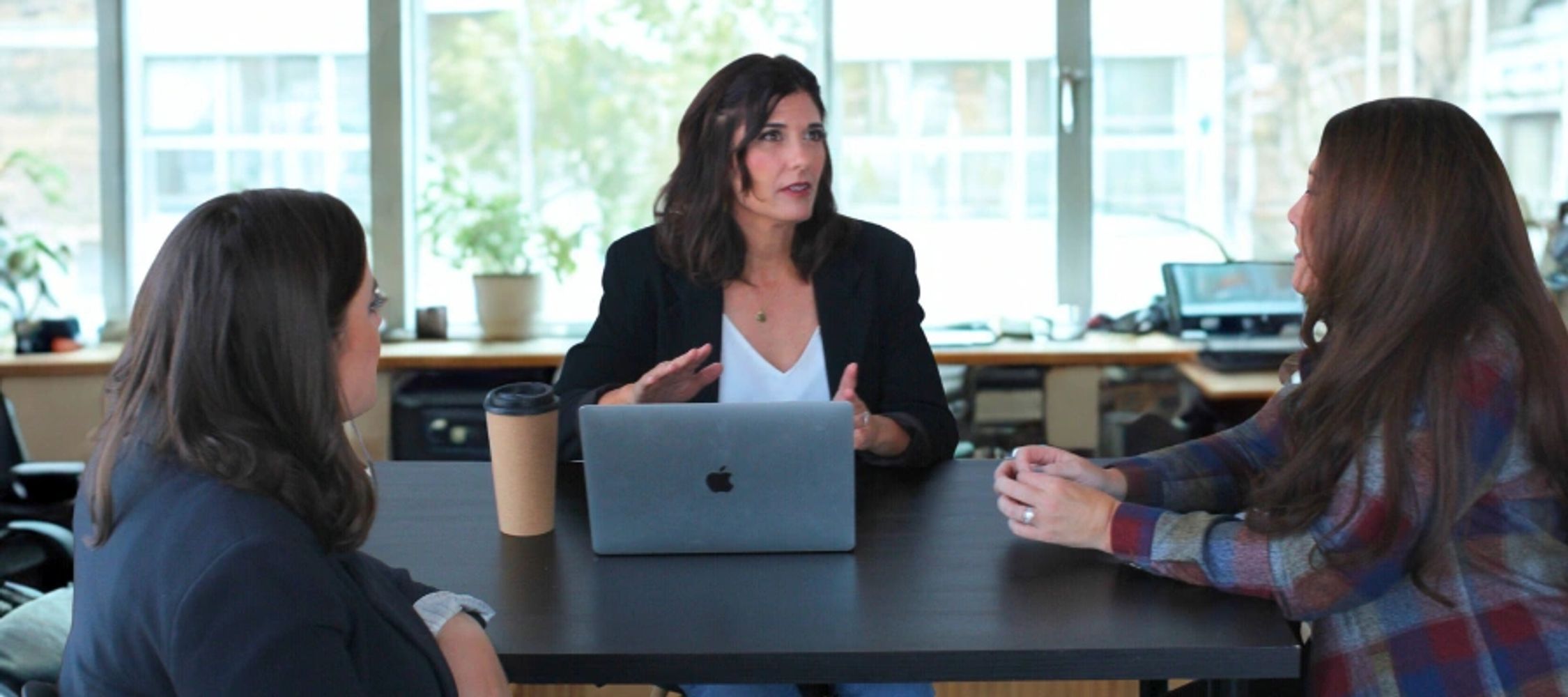 three women at a table with a large window behind them.