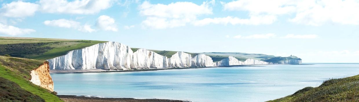 White chalk cliffs along a calm coastal shoreline under a bright sky.