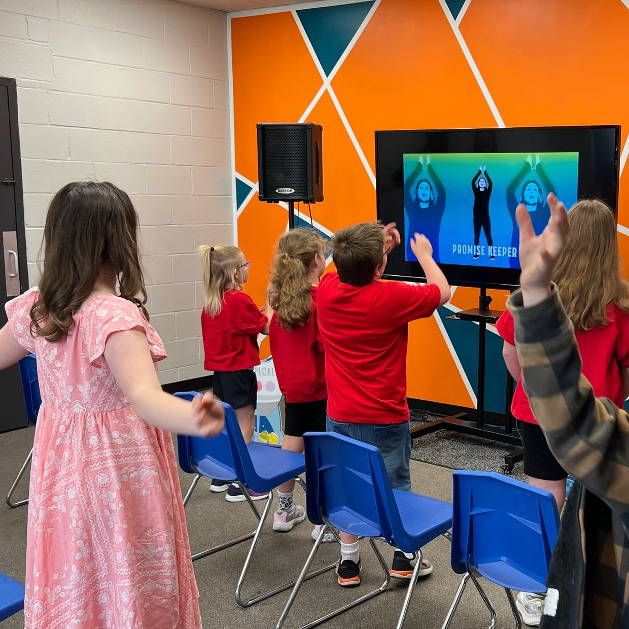 Children mimicking hand movements from a screen video titled 'Promise Keeper'.