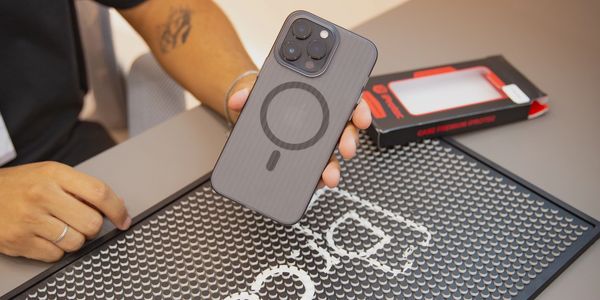 Person holding a smartphone with a MagSafe-compatible case over a branded mat.