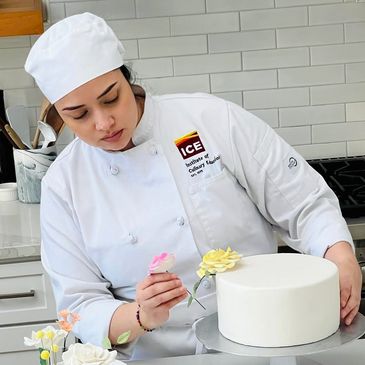 Pastry chef decorating a cake with icing flowers.