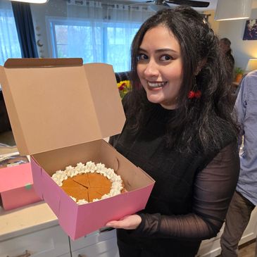 Woman smiling holding a cake in a pink box.