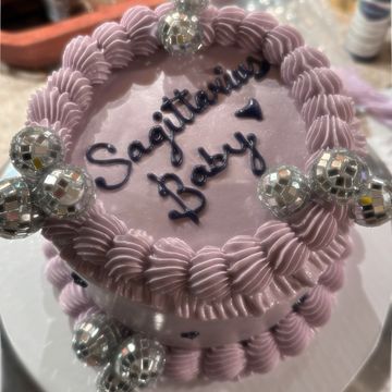 Purple cake with 'Sagittarius Baby' written and disco ball decorations.