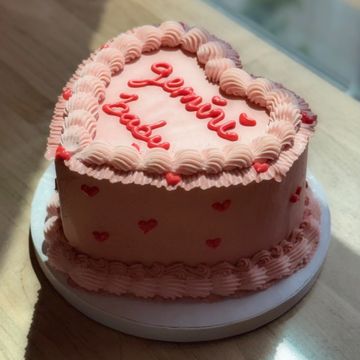 Heart-shaped pink cake with "genie bodo" written on top.