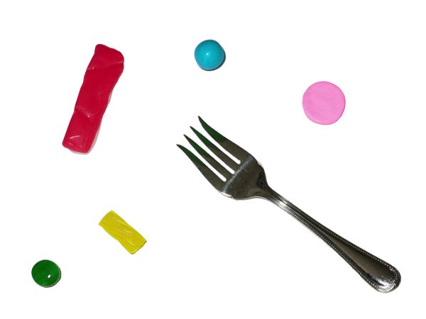 A fork surrounded by colorful candies and gum pieces on a white background.