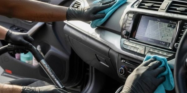 Two hands cleaning a car interior with cloths and a vacuum.