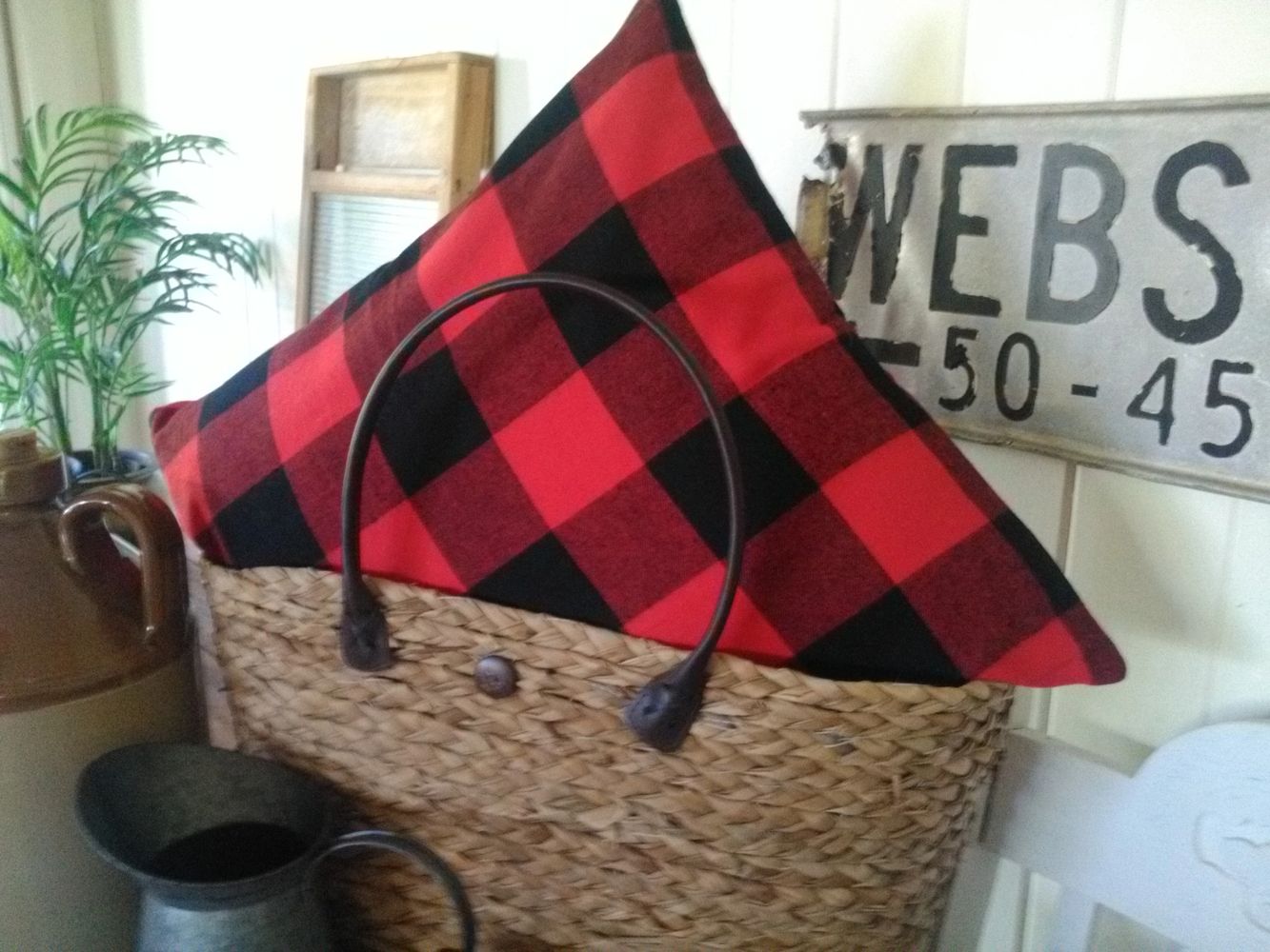 A woven basket with a red and black checkered pillow inside.