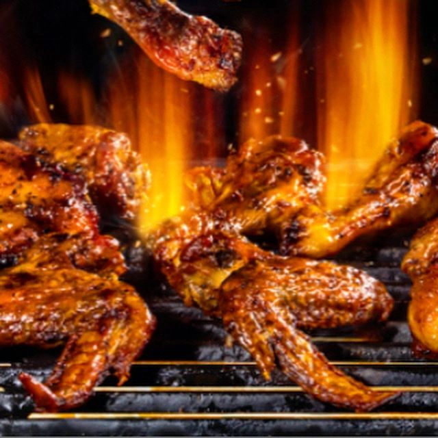 Spicy chicken wings grilling over open flames on a barbecue.