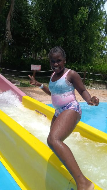 Girl enjoying a water slide at a pool on a sunny day.