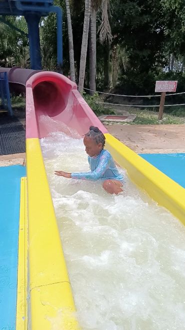 Child enjoying a water slide in a sunny outdoor pool area.