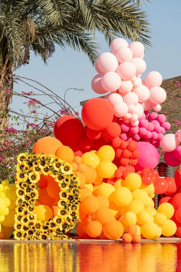 Colorful balloon arrangement with a sunflower-decorated letter D by a reflective pool.
