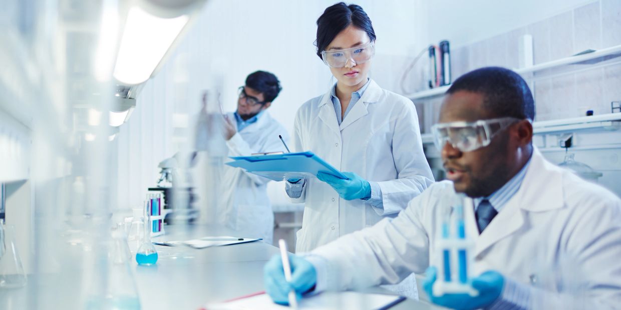 Scientists in lab coats working with blue liquid samples and taking notes in a laboratory.