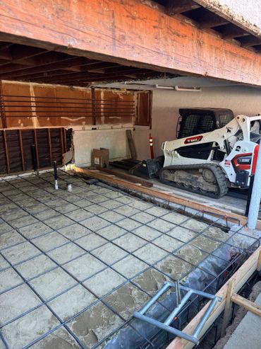 Construction site with foundation rebar and a Bobcat loader inside a building.