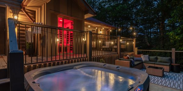 Cozy outdoor patio with hot tub, lounge seating, and warm lighting at dusk.