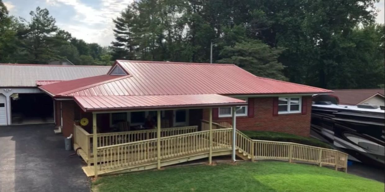 A brick house with a red metal roof and a wooden ramp porch.