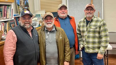 Four smiling men in casual outdoor clothing posing indoors.