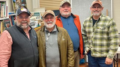 Four smiling men in casual outdoor clothing posing indoors.
