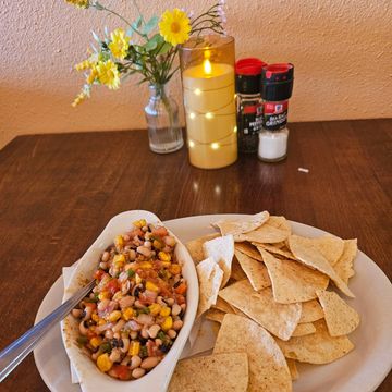 A plate with tortilla chips and a bean salad on a wooden table with candle and flowers.