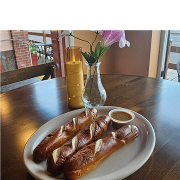 Three pretzel sticks with mustard dip on a white plate at a cozy table.