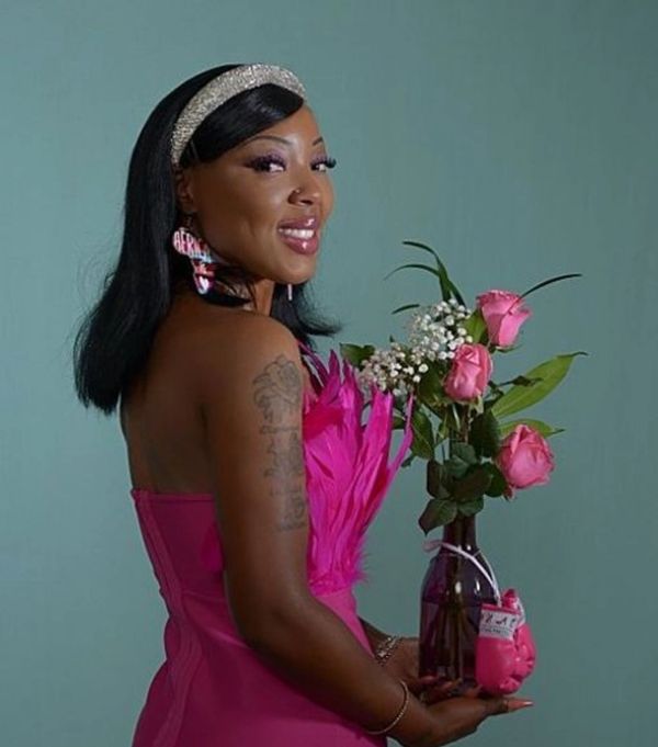 Woman in pink dress holding a vase of pink roses, smiling.
