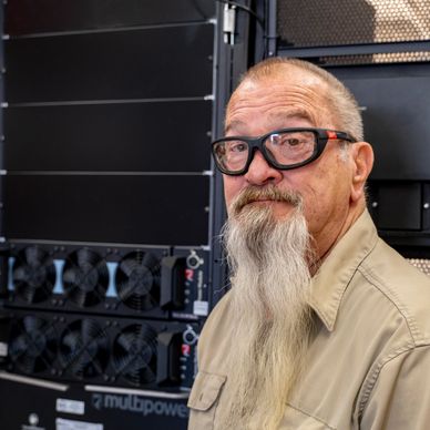 Older man with long beard and glasses near computer hardware.