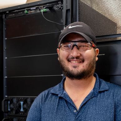 Man wearing safety glasses and a cap smiling in a server room.