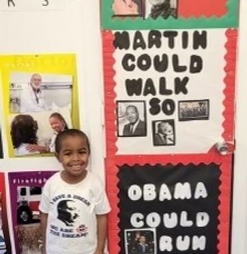 Young boy stands smiling beside a door decorated with civil rights leaders' achievements.