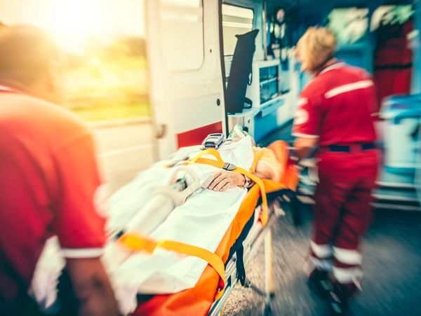 Paramedics rush a patient on a stretcher into an ambulance during sunset.