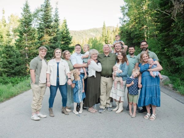 A large family posing together outdoors on a road surrounded by trees.