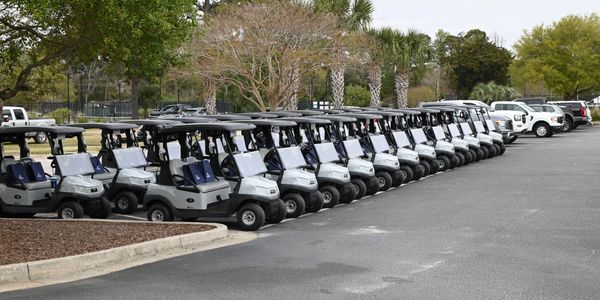 A row of parked golf carts lined up in a parking lot.