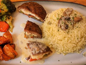 Plated meal with rice, stuffed meat, roasted potatoes, and mixed vegetables.