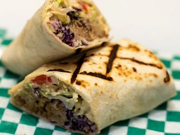 Grilled wrap sandwich filled with meat and fresh vegetables on checkered paper.