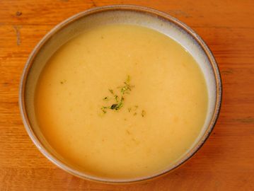 Creamy bowl of soup garnished with herbs on wooden table.