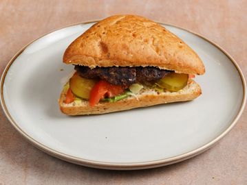 Grilled burger sandwich with pickles and tomatoes on a white plate.
