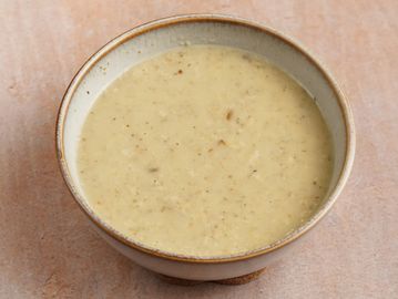 A bowl of creamy mushroom soup on a beige surface.