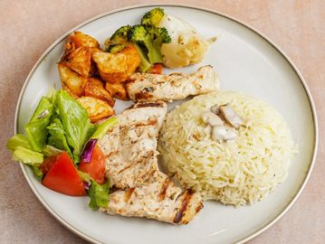 Grilled chicken with rice, roasted potatoes, steamed vegetables, and salad on a plate.