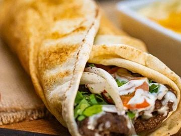 Close-up of a delicious grilled wrap with meat, veggies, and creamy sauce.