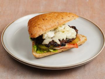Grilled cheeseburger sandwich with lettuce, pickles, and tomato on a white plate.