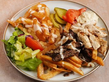 Plate with fries, grilled chicken, beef, salad, tomato, pickles, and sauce.