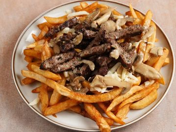 Plate of fries topped with grilled beef, mushrooms, and sauce.