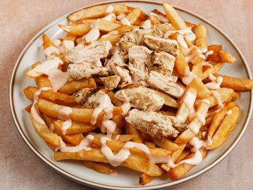 Plate of crispy fries topped with grilled chicken and drizzled with creamy sauce.