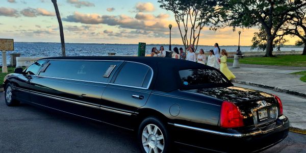 Black stretch limousine parked by the waterfront during sunset.
