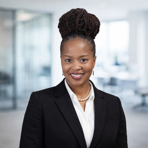 Professional woman in a black blazer with a pearl necklace smiles confidently.