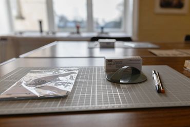 A workspace with a cutting mat, eraser, pen, and a packaged item.