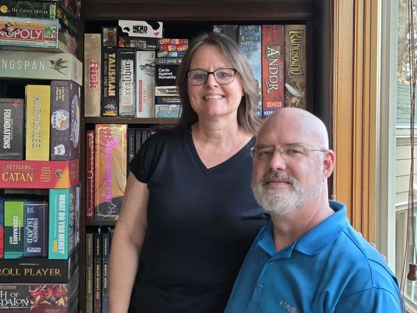 A picture of Jeremy and Suzanne Hegarty in front of a shelf full of board games.