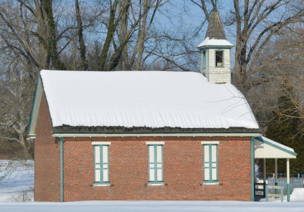 Snow-covered small brick church with white and teal accents in winter.